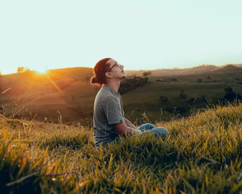 Mann mit geschlossenen Augen sitzt auf einem Grasfeld