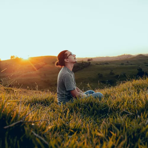 Mann mit geschlossenen Augen sitzt auf einem Grasfeld